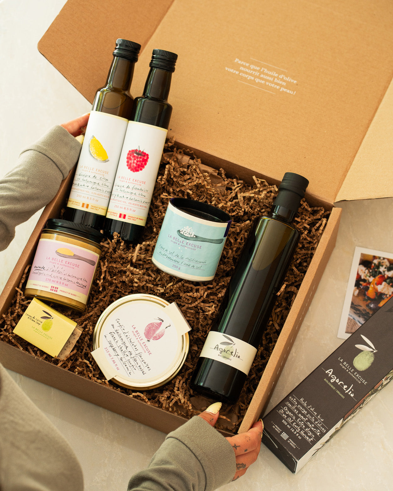 A curated La Belle Excuse gourmet gift box featuring organic Agorelio olive oil, lemon and raspberry white balsamic vinegars, French shallot confit, roasted garlic mustard, Mediterranean fleur de sel, and rosemary, lemon and coffee kitchen soap.